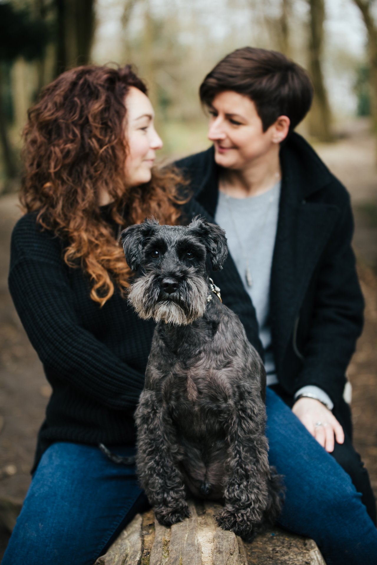Two gorgeous ladies smiling with their dog during their engagement shoot in a woodland setting in Kent