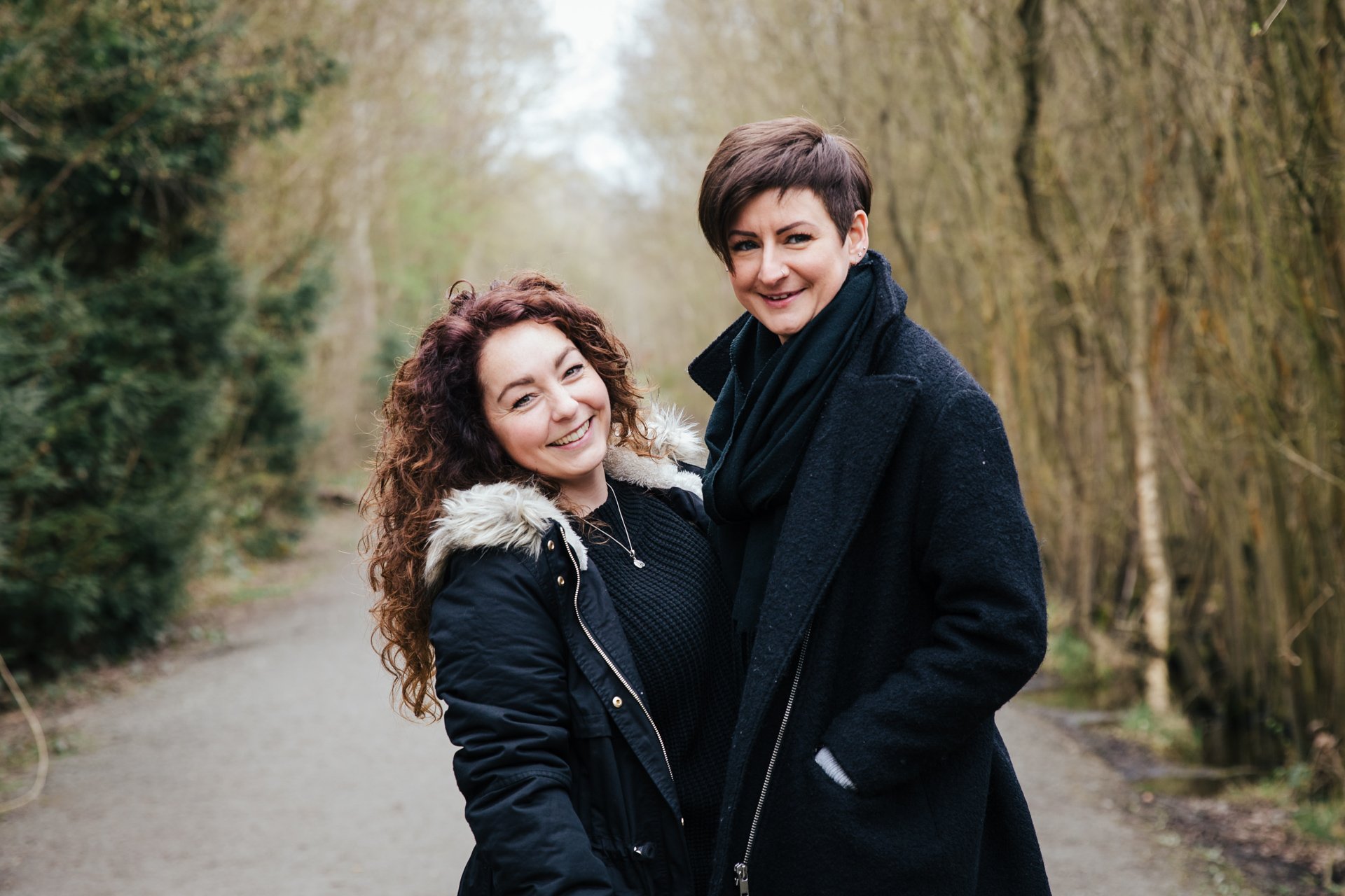 Two gorgeous ladies smiling during their engagement shoot in a woodland setting in Kent