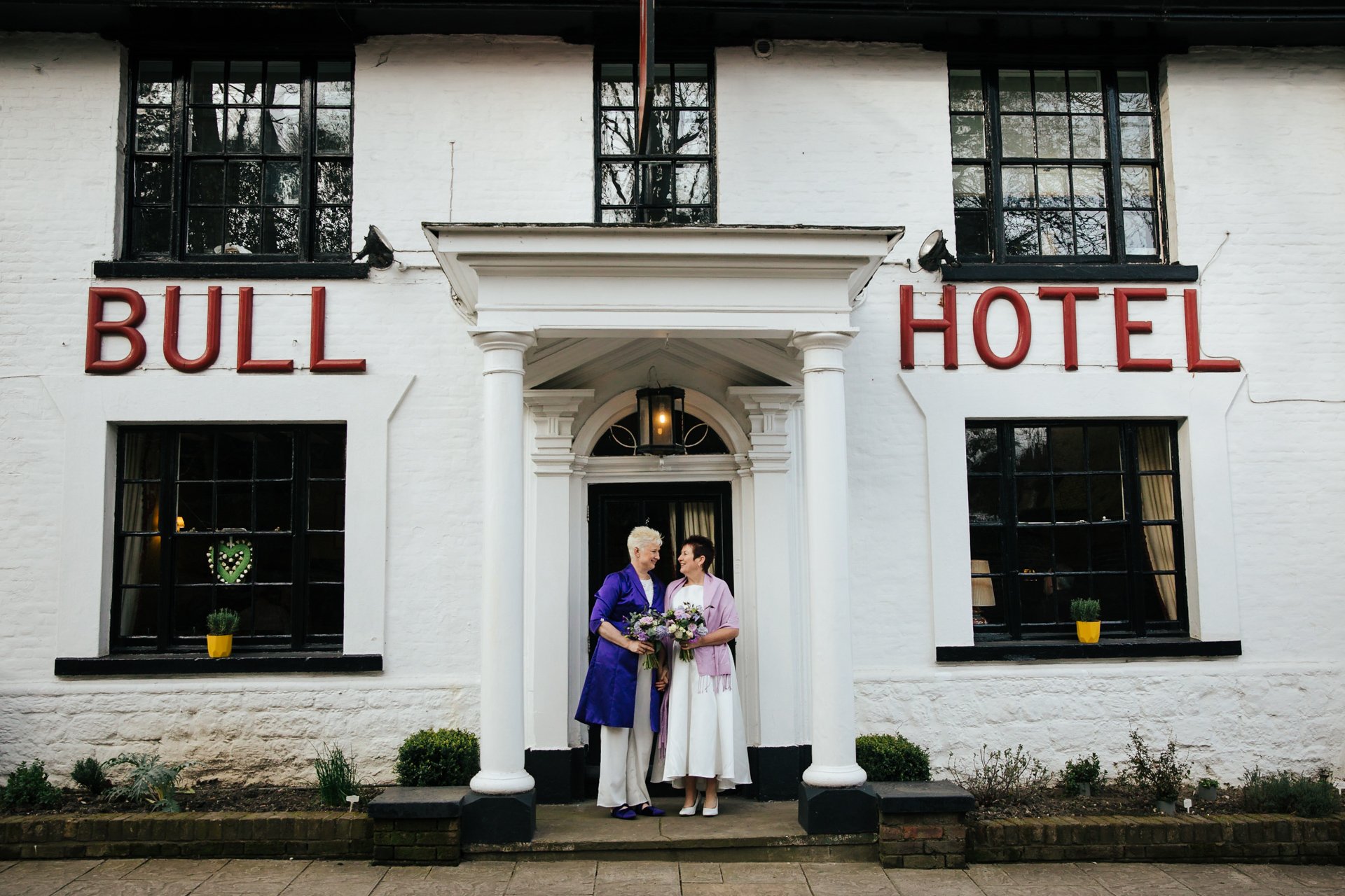 Two brides happy and smiling at each other outside their Kent wedding venue