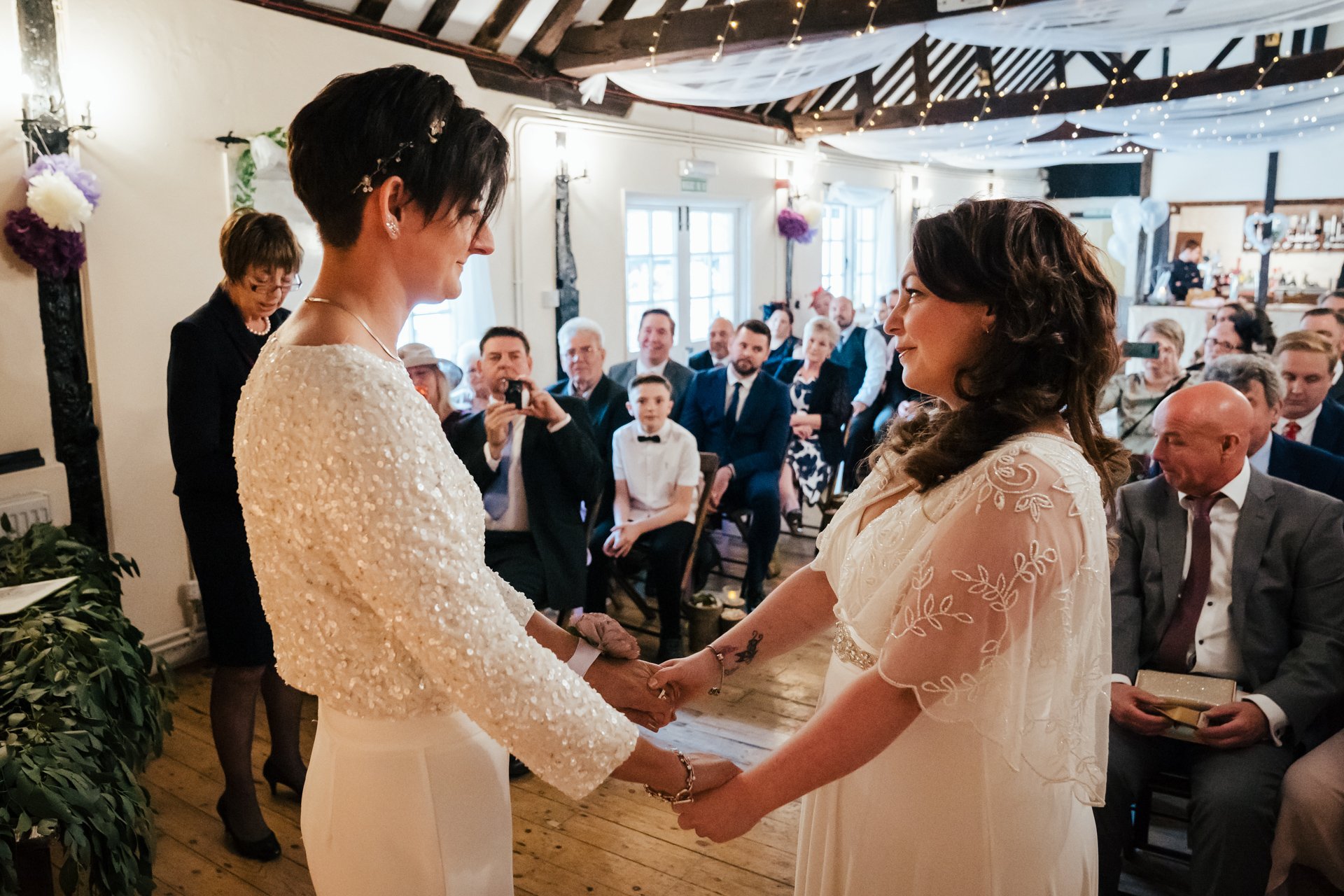 Two Brides holding hands together infant of their guests in their wedding ceremony at The Bull Hotel, Kent
