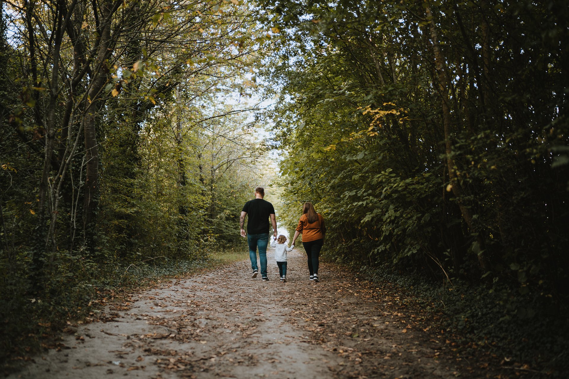 Engaged couple and their daughter walking through woodland at Lullingstone Country Park Kent