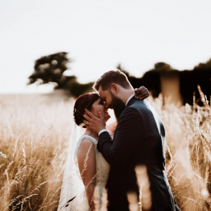 Bride and Groom node to nose and smiling in a field during sunset