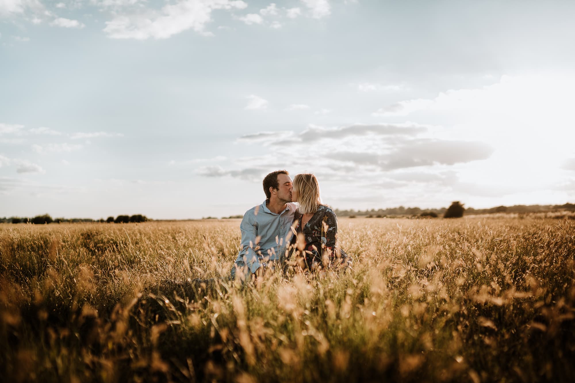 Couple seated in long grass during sunset kissing each other