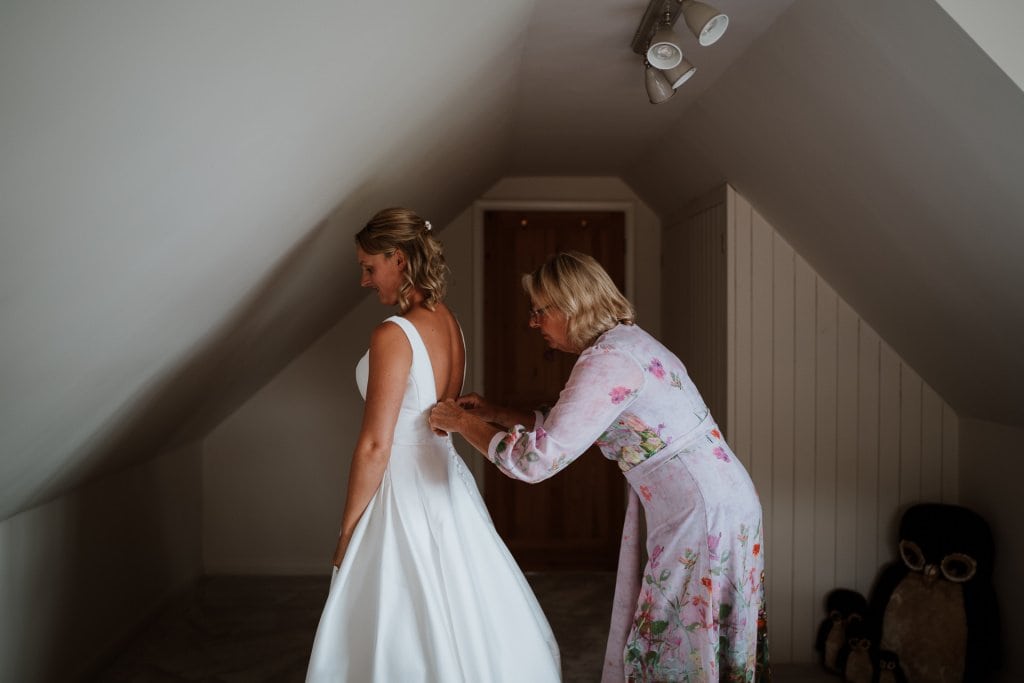 Bride being assisted by her mother to fasten the back of her stunning wedding dress