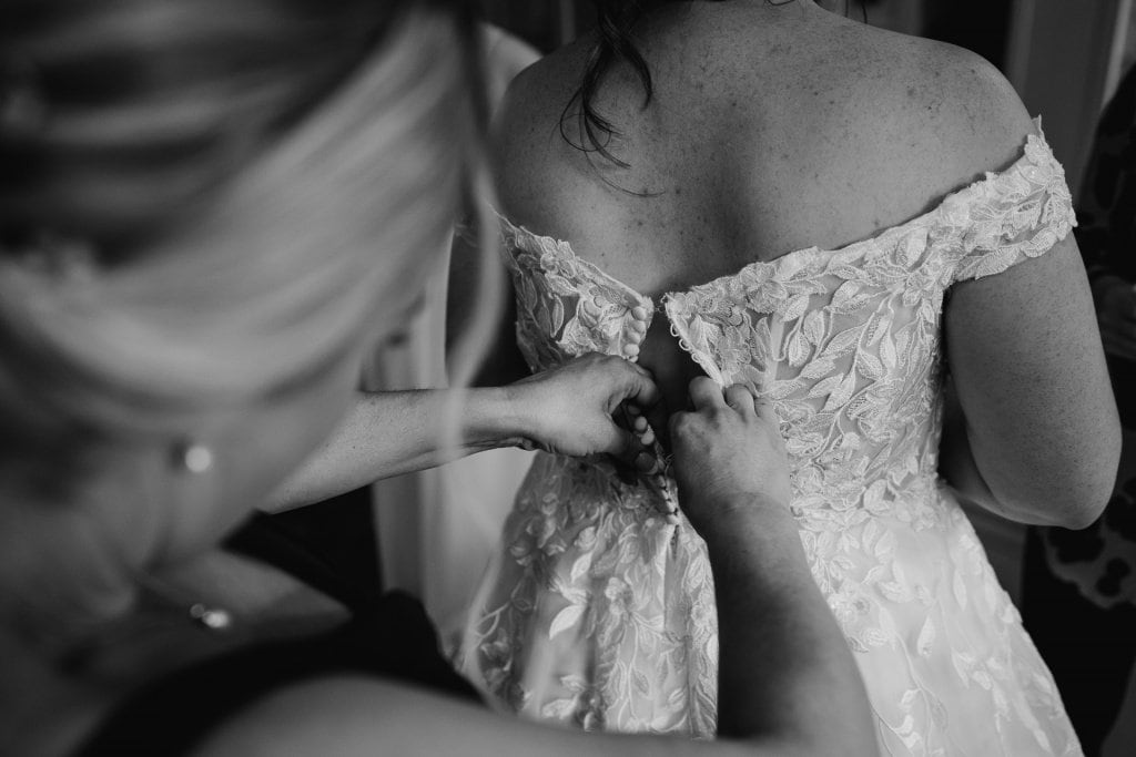 Black and white image of the back of a wedding dress being fastened by a bridesmaid