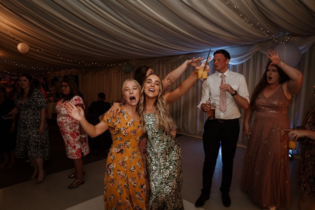 Wedding guests with arms raised dancing and singing on the dance floor