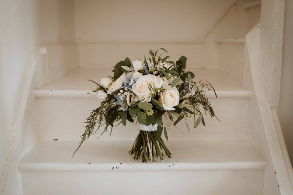 Stunning white rode and eucalyptus bouquet on a white wooden staircase