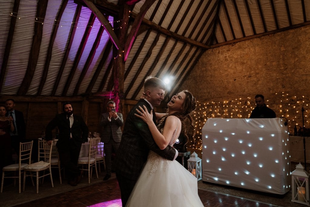 Bride laughing being held by groom during their first dance