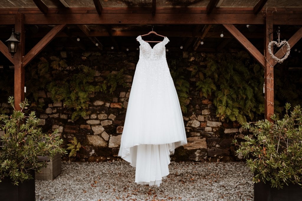 White wedding dress suspended in front of rustic brick backdrop