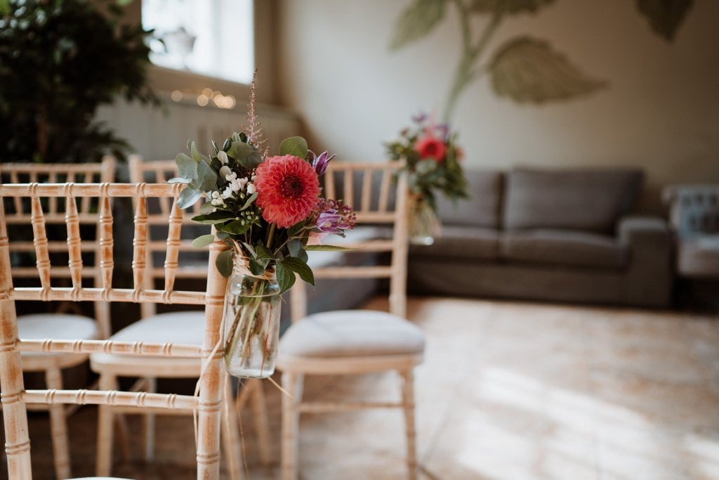 Wedding ceremony chair decorated with a glass jar filled with pink flowers