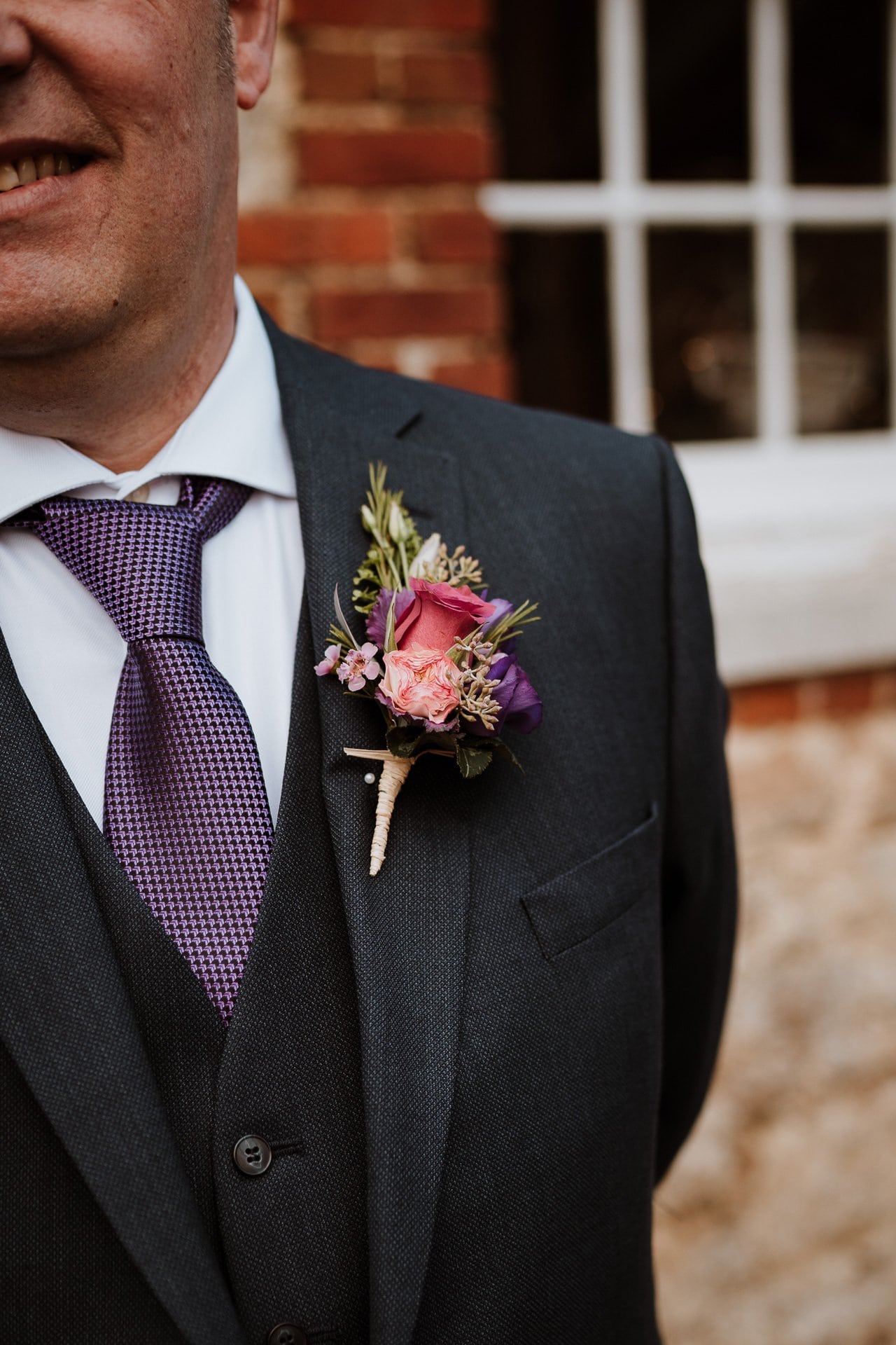 Close up image of grooms button hole with pink and purple flowers