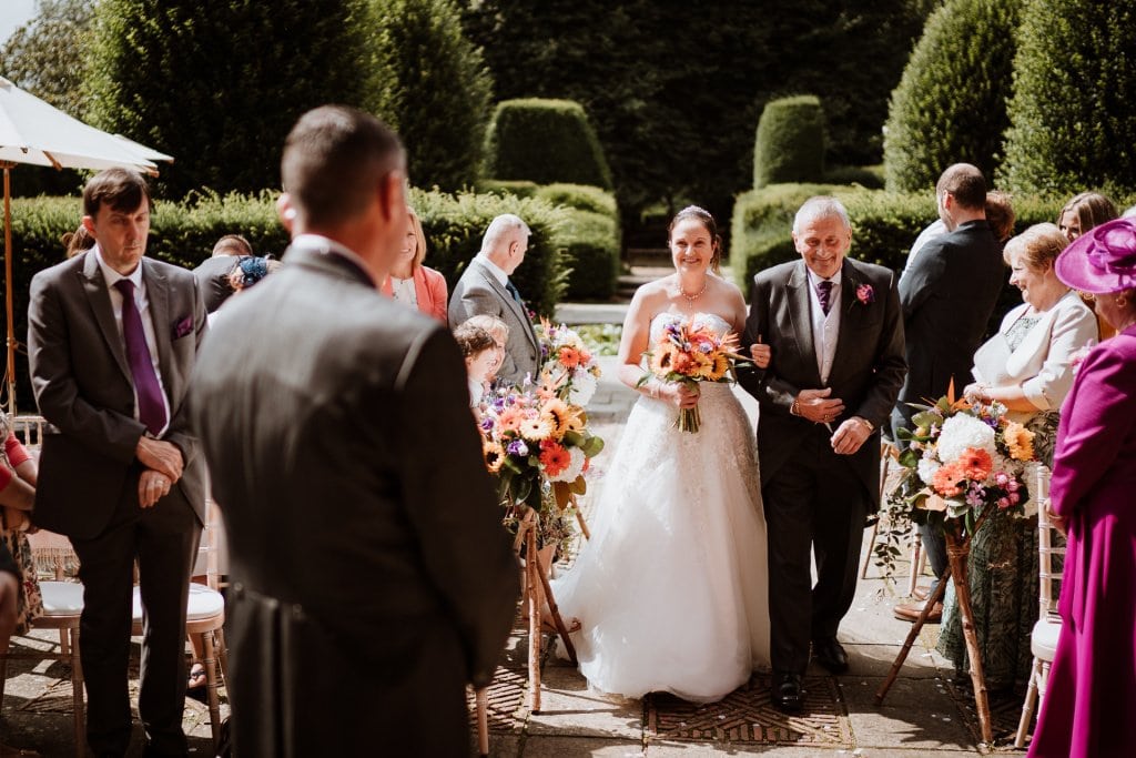 Bride accompanied by her father being walked down the aisle towards her waiting husband to be