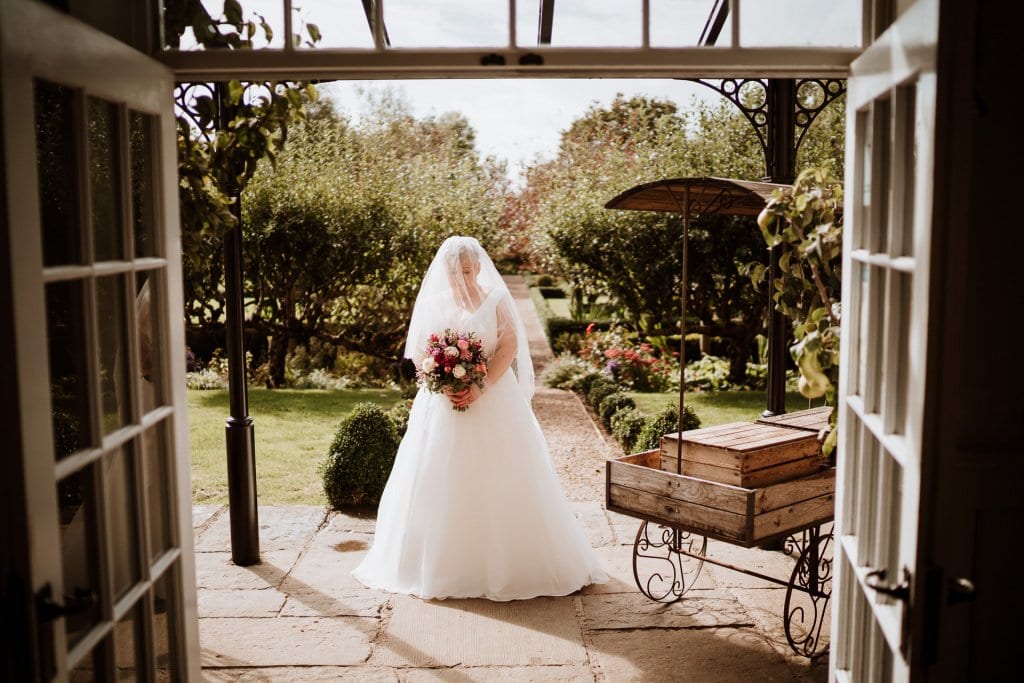 Bride with veil over her head holding her bouquet framed by open doorway
