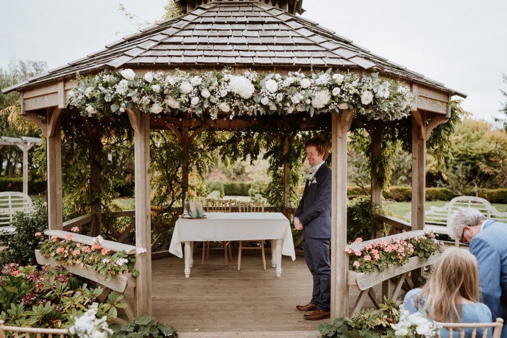 Groom waiting nervously for his bride, standing under the gazebo at the Secret Garden