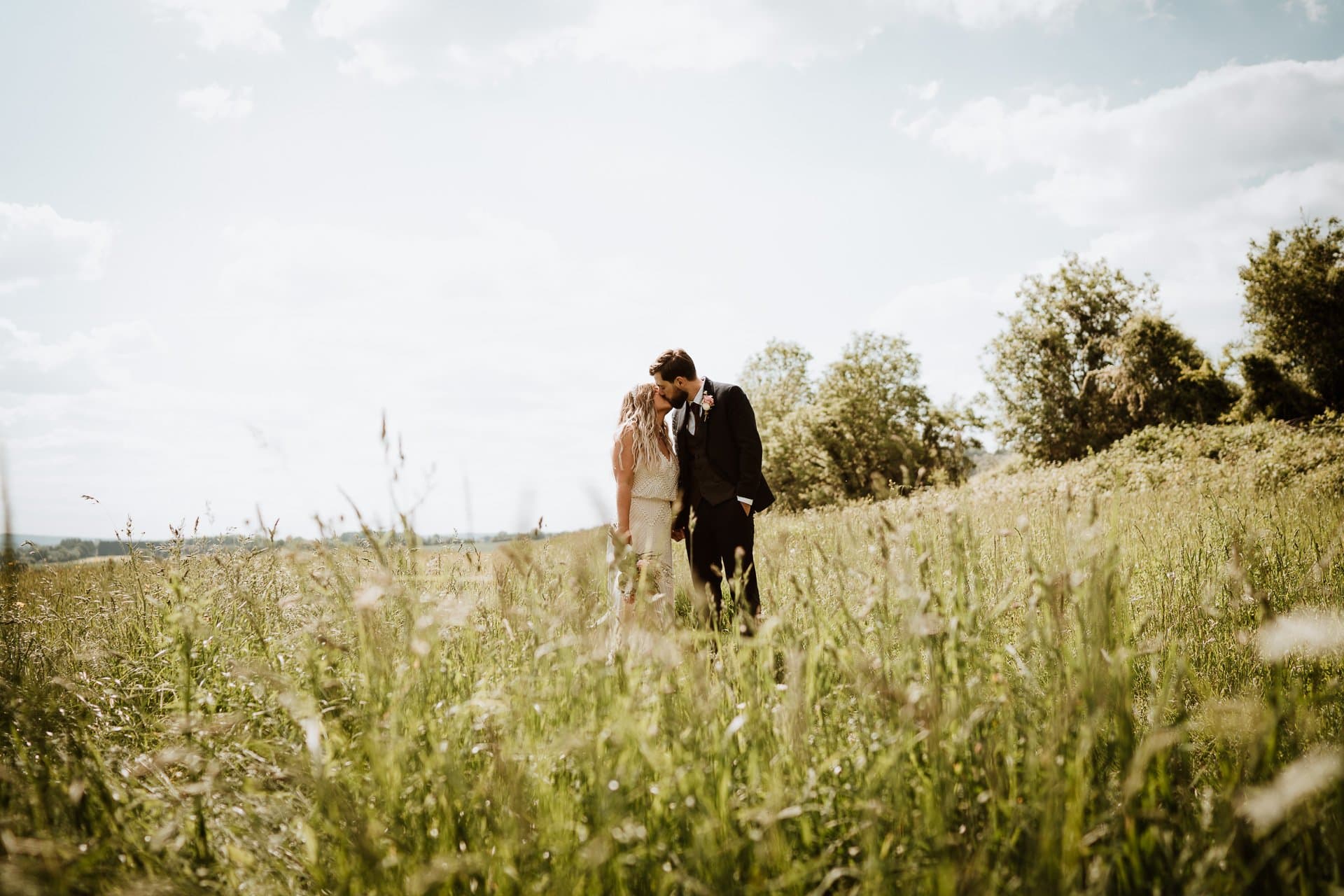 Bride and Groom kissing in field of long grass in Kent countryside