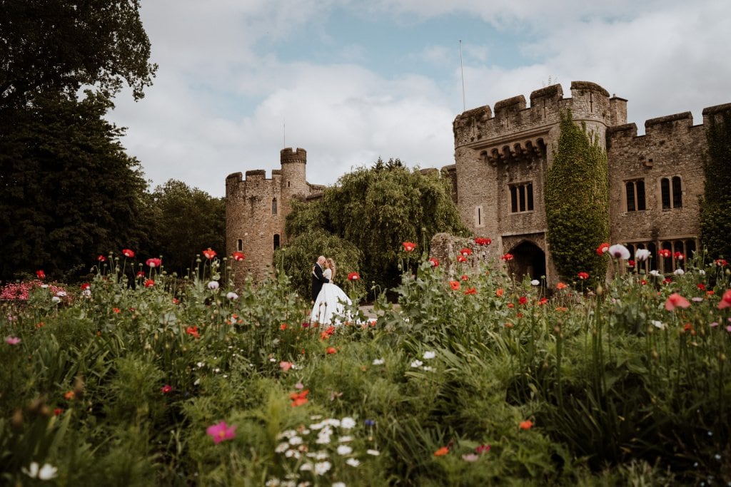 Bride and Groom on front of Allington Castle, Kent wedding venue through a bed of poppies