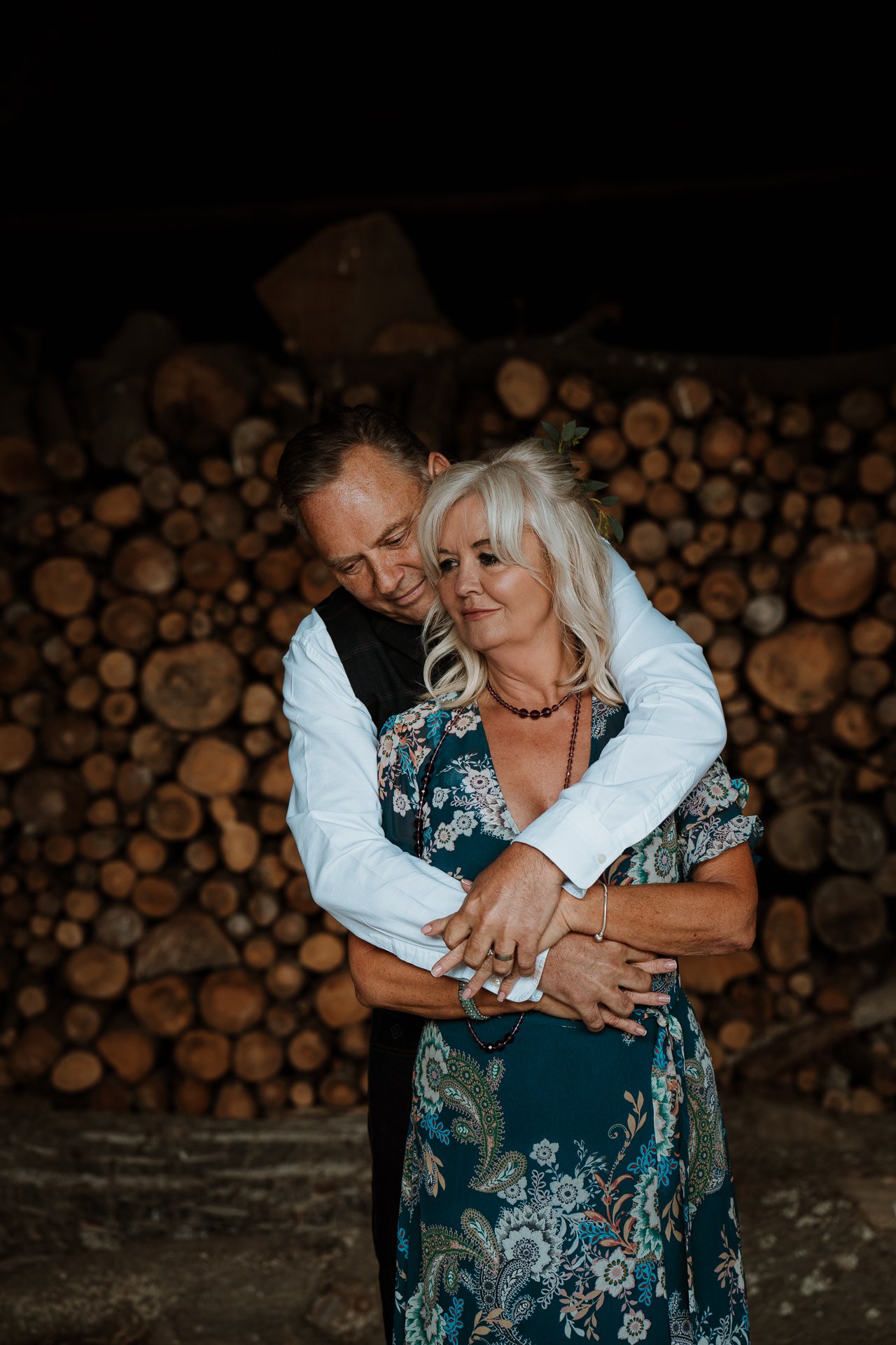 Groom with his arms wrapped around his bride in front of wood stack in the barn at The Oak barn