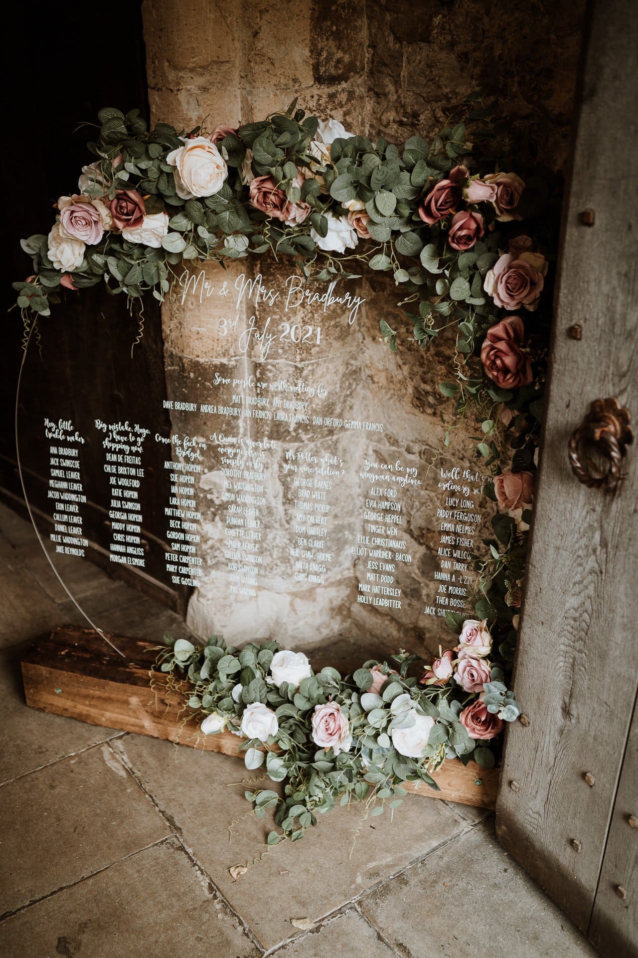 Round acrylic table plan with white calligraphy and dressed with light and dusky pink roses and green foliage