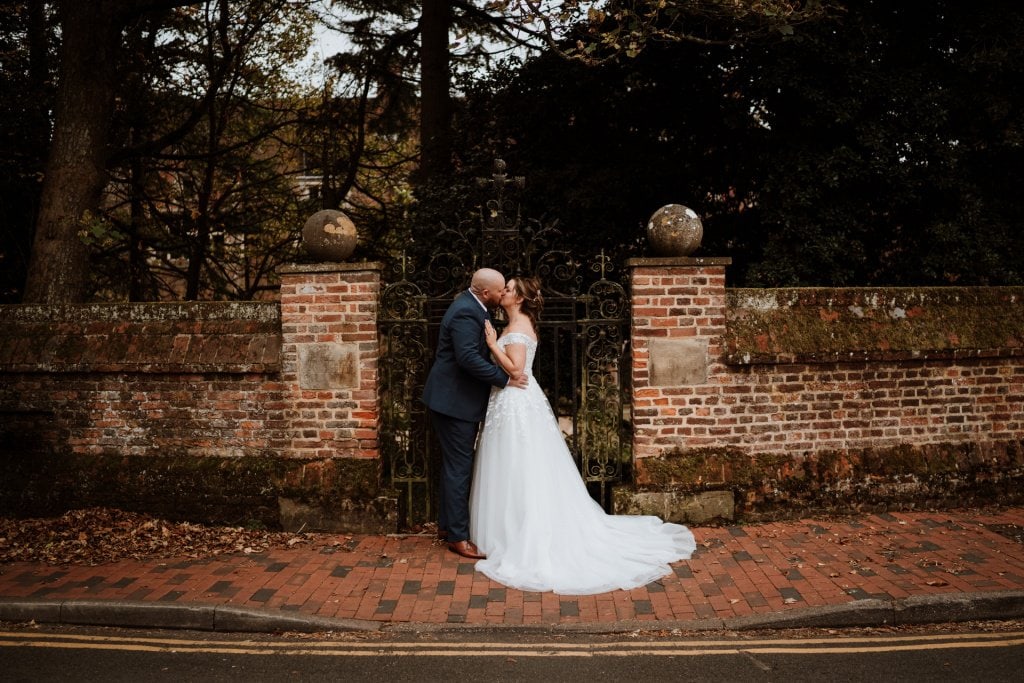 Bride and Groom kissing in front of wrought iron gate and red brick wall in Wrotham Village Kent