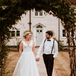 Bride in white dress with hand in pocket walking with her Groom in Black tie at Blake Hall Wedding venue