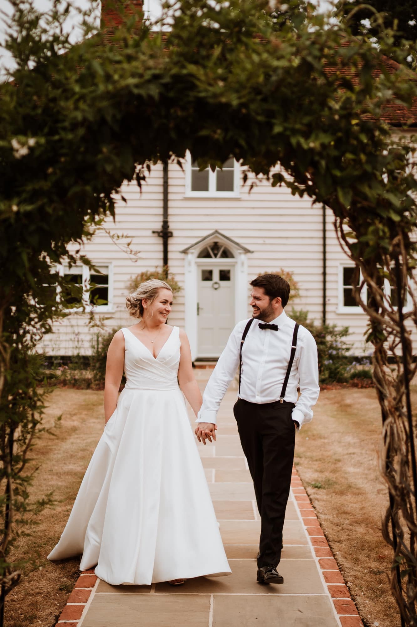 Bride in white dress with hand in pocket walking with her Groom in Black tie at Blake Hall Wedding venue