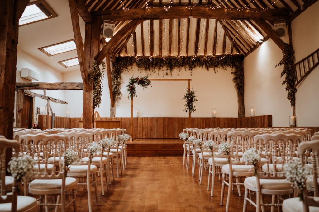 The interior of the wedding barn at Winters Barns Wedding venue with chairs dressed with white flowers