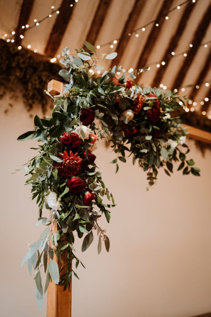Red and white flowers and green foliage adorns a wooden hand made wedding arch