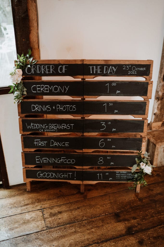 Wooden pallet and chalkboard wedding day timeline with green and white flowers
