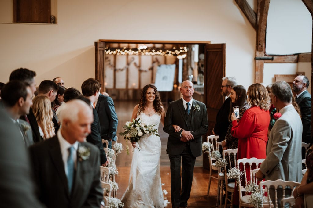 Bride arm in arm with her dad as she walks down the aisle at Winters Barns