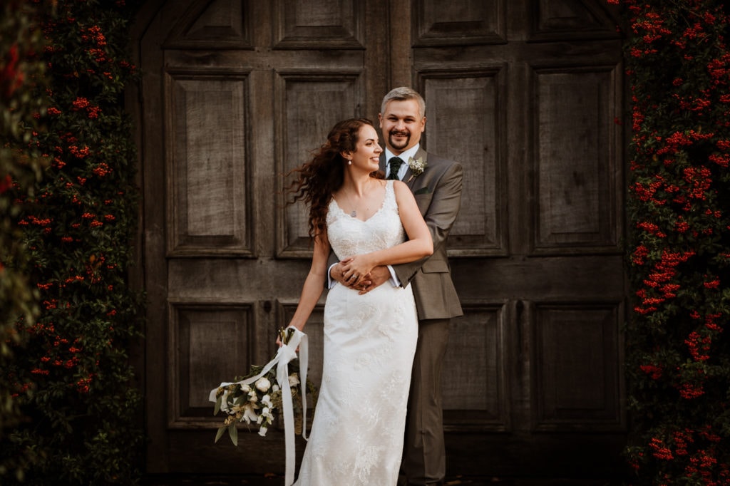 Groom holding his Bride at the waist at the wooden doors of Winters Barn Kent Wedding Venue