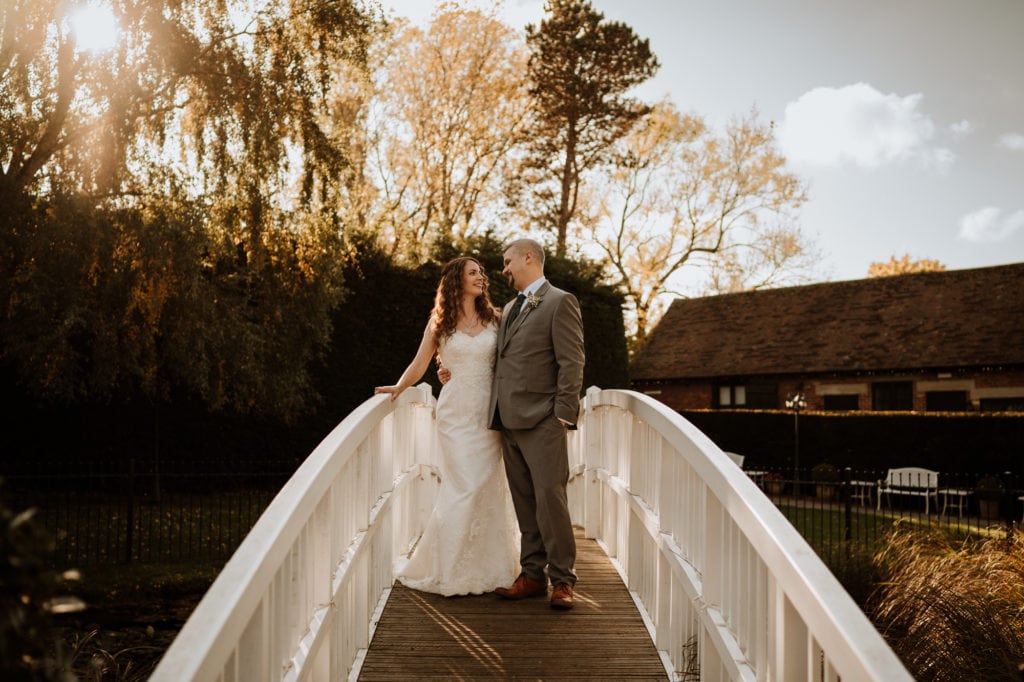 Bride and Groom standing together looking relaxed on the white bridge over the pond at Winters Barns