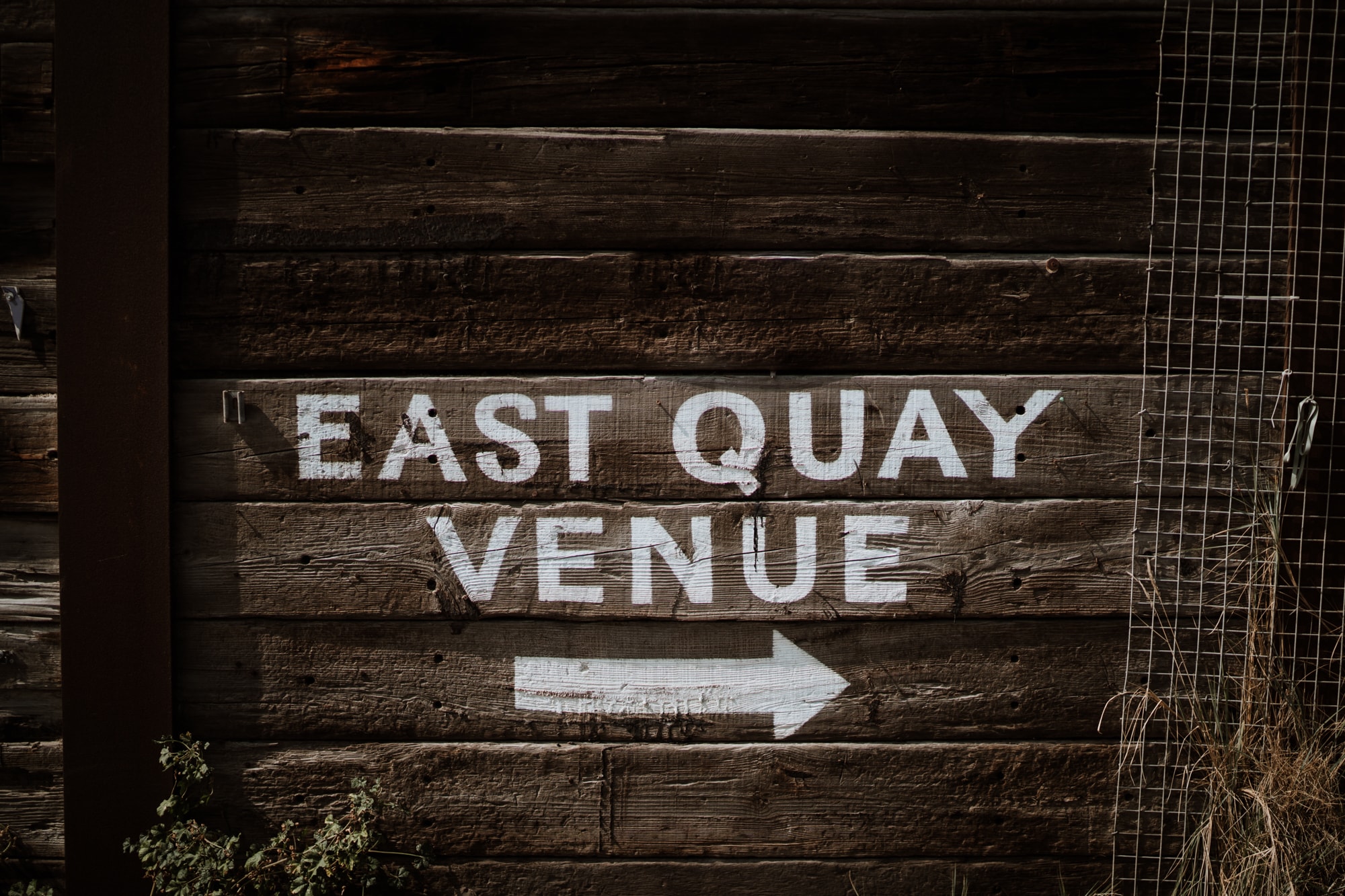 Wall made of black sleepers with East Quay Venue written in white paint
