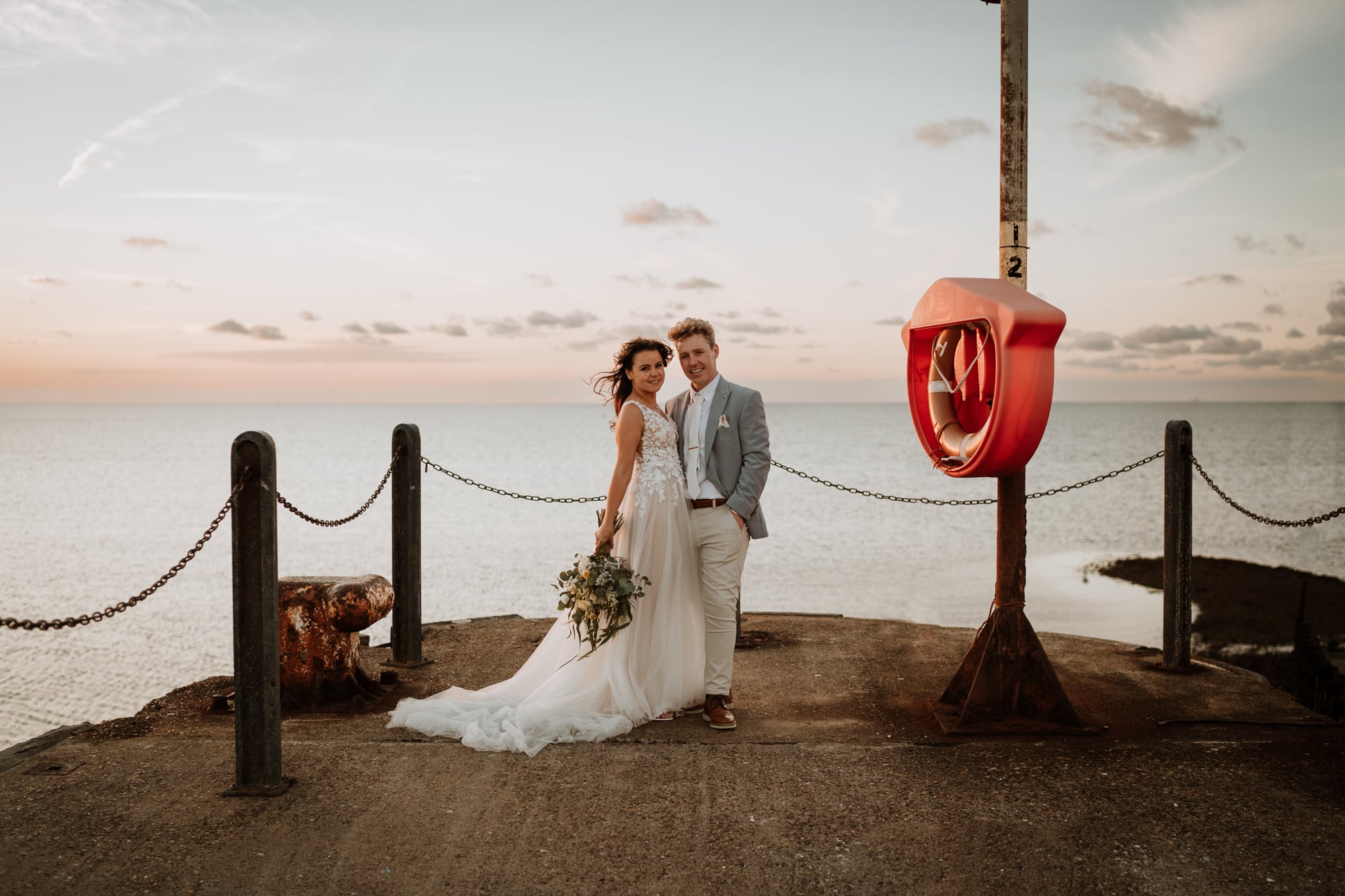 Bride and groom looking relaxed at the end of the jetty at East Quay as the sun sets