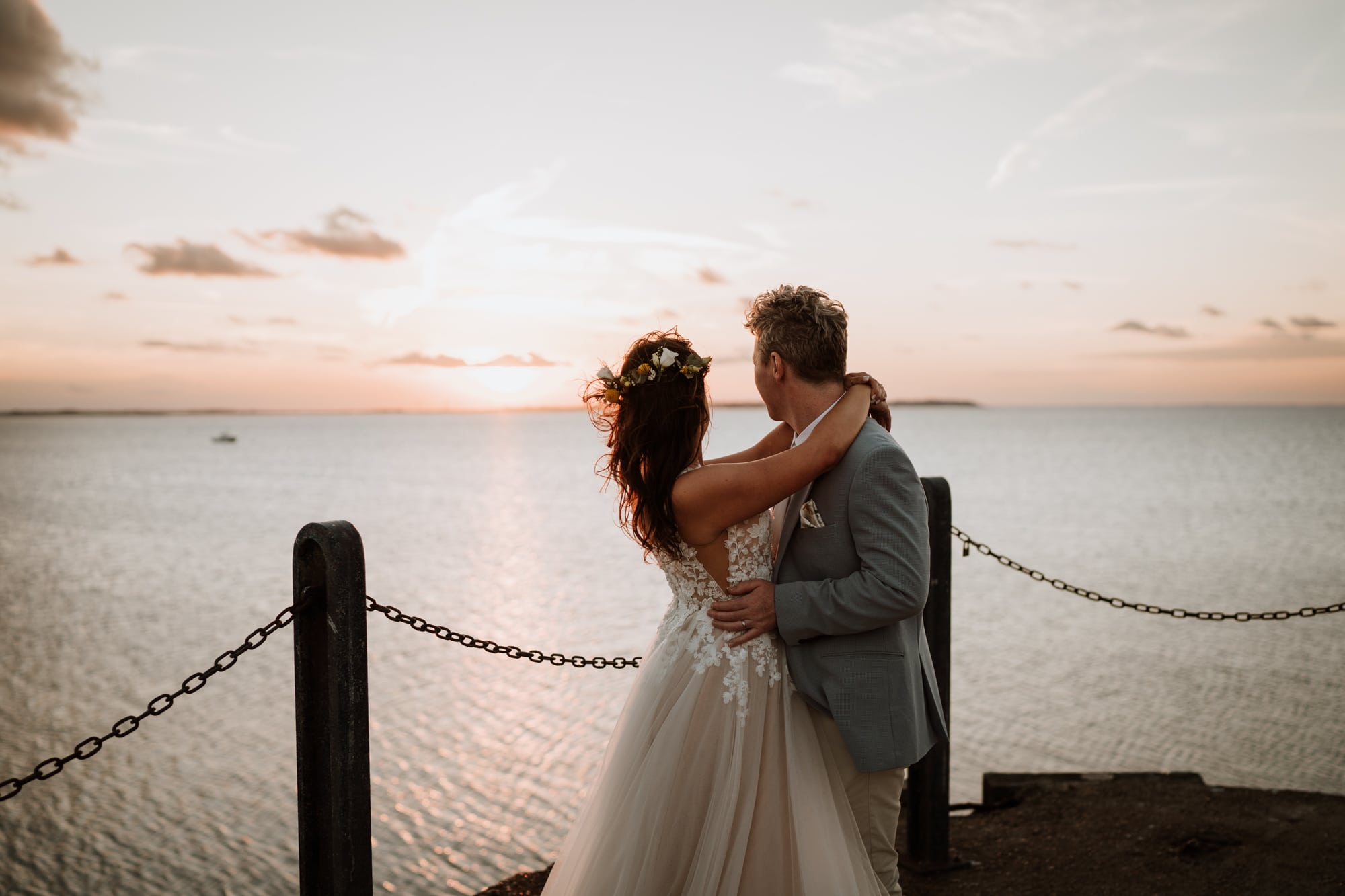 Bride and groom with their arms around each other watching the sun go down at their kent wedding venue east quay