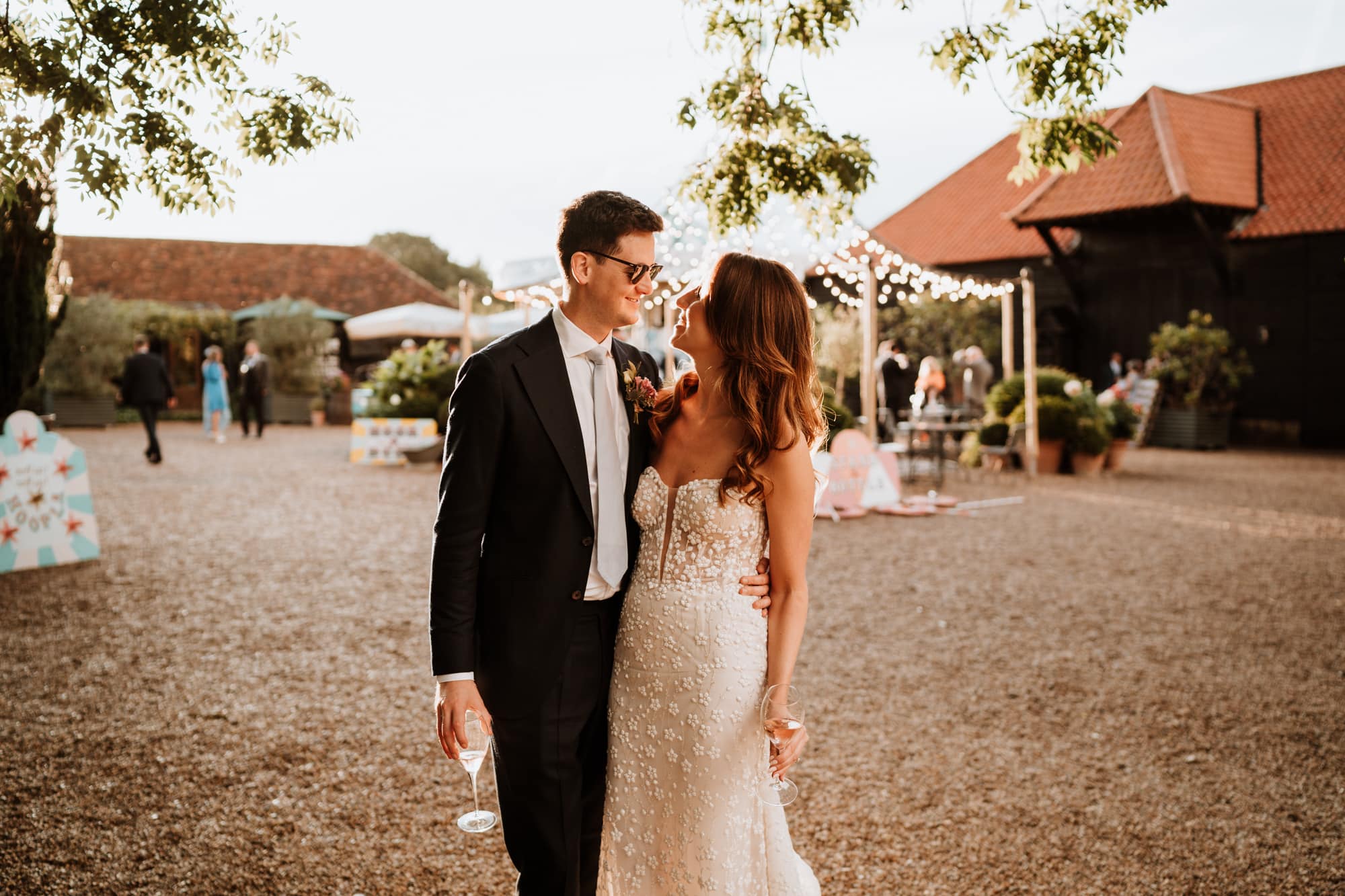 Relaxed Bride and Groom with glass in hand and sunglasses on smiling at each other with a carousel in the background