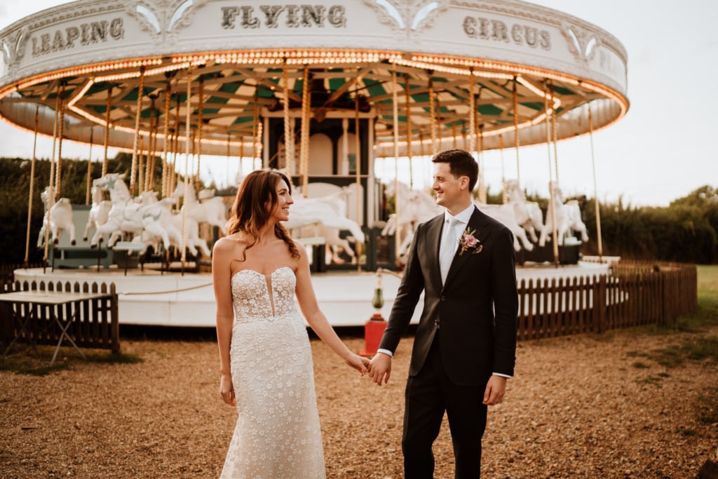 The couple standing in front of the carousel ride at Preston Court in Canterbury which is a wedding venue in Kent