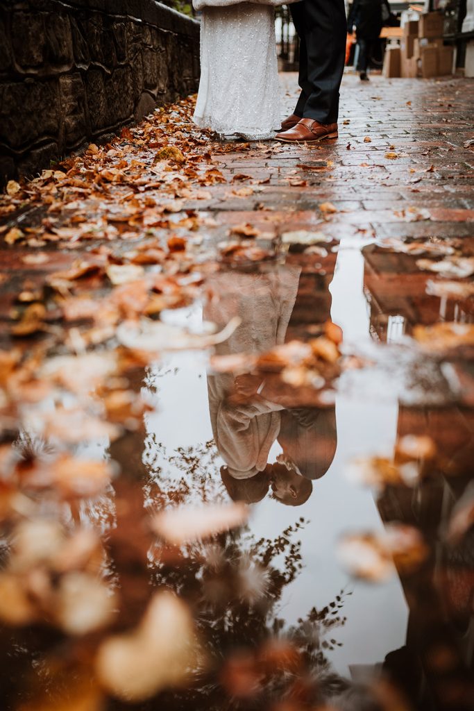 Couple on the rainy wedding day reflected ina puddle