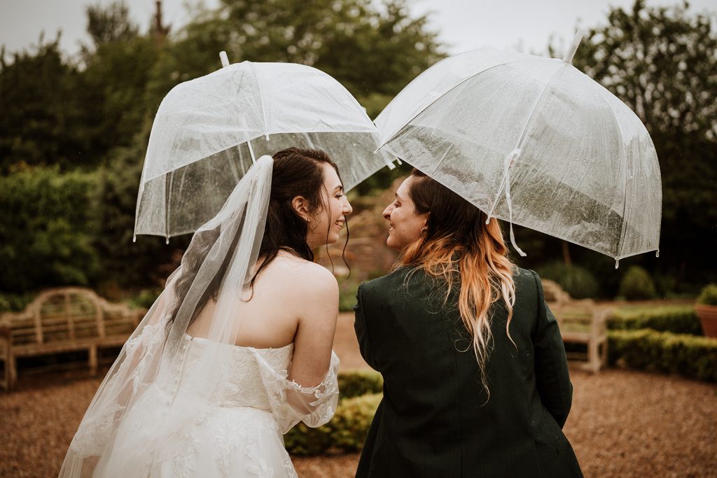 couple smiling under clear umbrellas during their rainy wedding day
